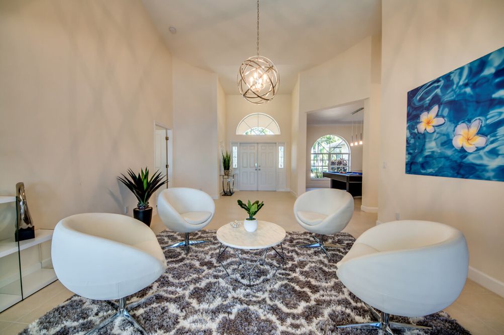 Blick vom formalen Wohnzimmer mit weißen Drehsesseln und dunklem Teppich in Richtung Eingangsbereich in der Villa Blue Pearl in Cape Coral, Florida